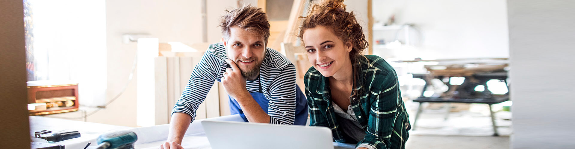Seguro de Responsabilidad Civil Autonomos - Pareja joven de autonomos sonriendo con un portatil mientras trabajan en una carpinteria Seguro de Responsabilidad Civil Autonomos - Pareja joven de autonomos sonriendo con un portatil mientras trabajan en una carpinteria
