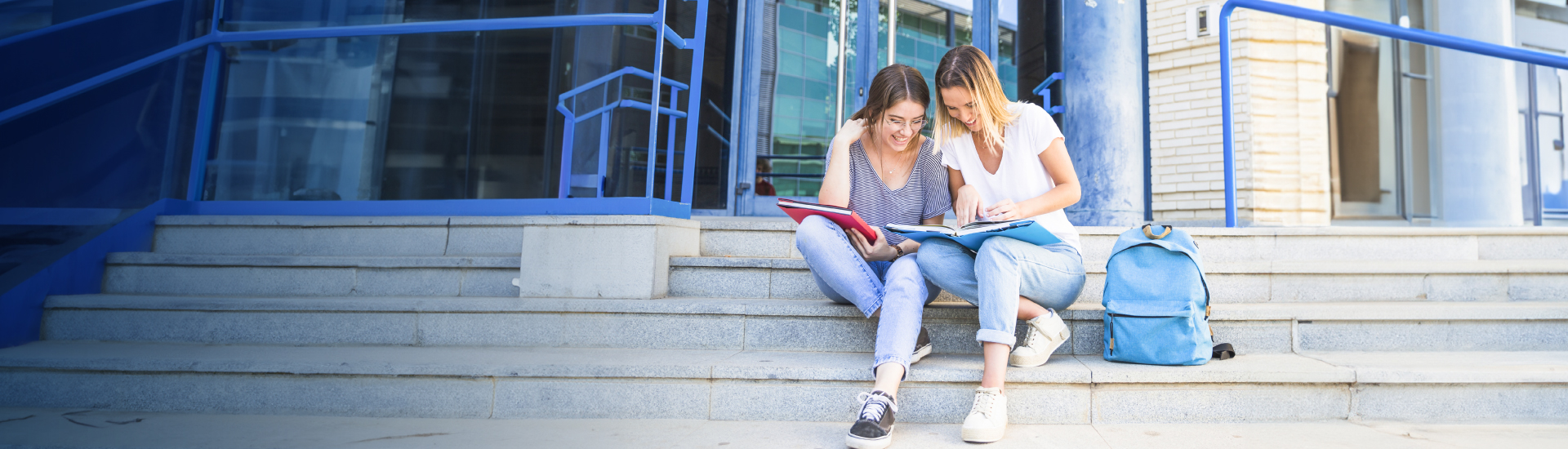 Préstamo universitario - Dos chicas sentadas en unas escaleras sonriendo mirando apuntes