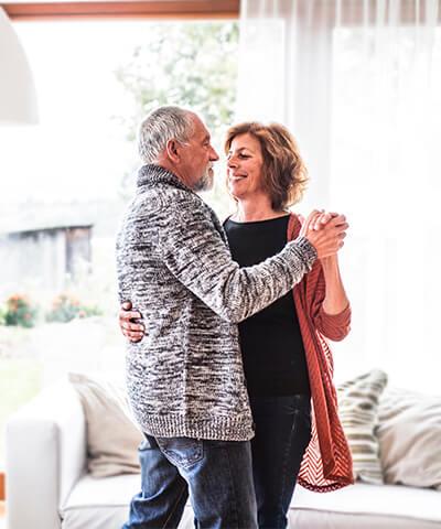 Modulo texto mi jubilacion - Pareja senior sonriendo y bailando en el salon de su casa