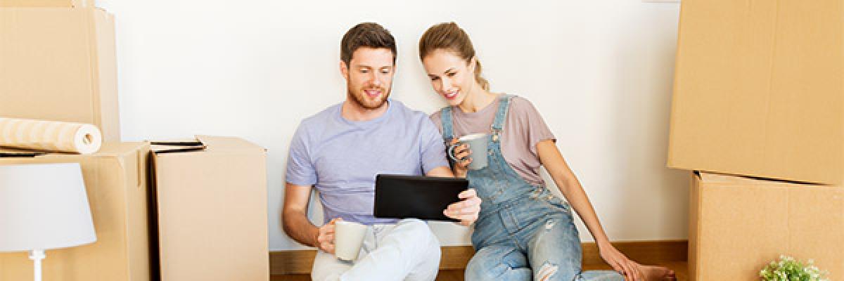 Hipoteca Vivienda - Una pareja sentada en el suelo entre cajas de mudanza con una tableta digital 