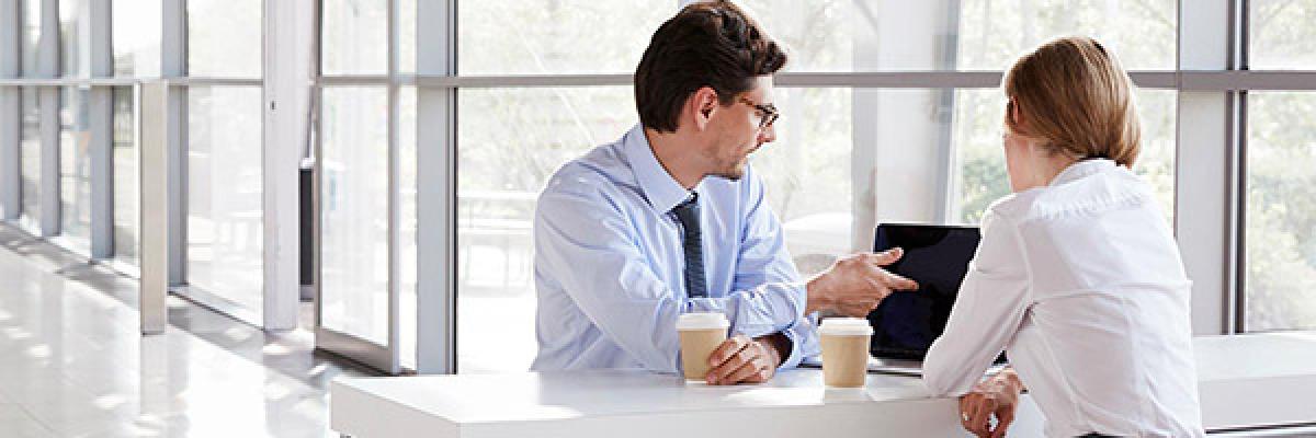 Financiación internacional - Reunión de negocios entre un hombre y una mujer de negocios con camisa, frente a un portátil hablando y tomando café