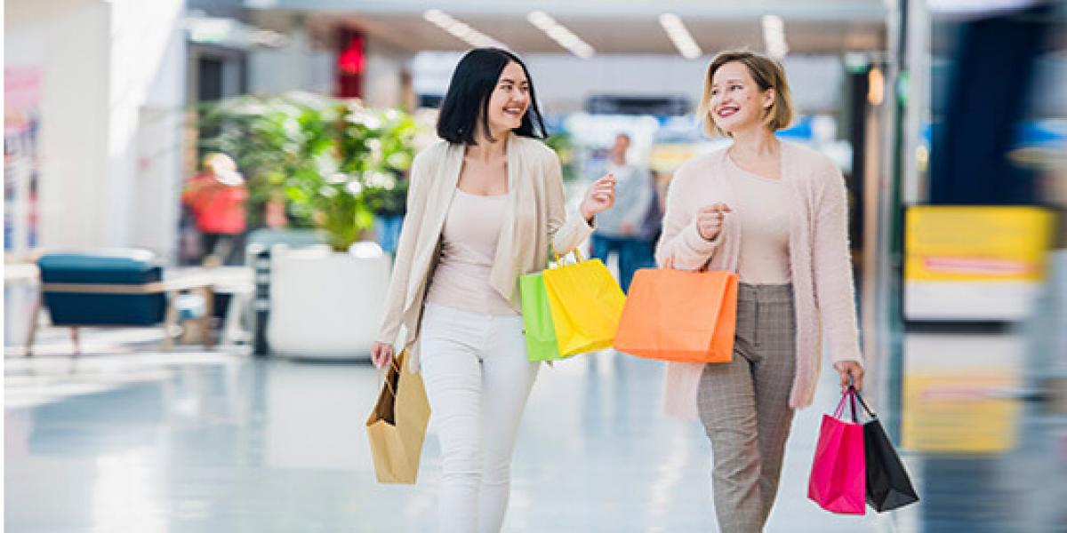 Finanzás - Dos mujeres hablando y sonriendo mientras están de compras con bolsas en las manos en un centro comercial